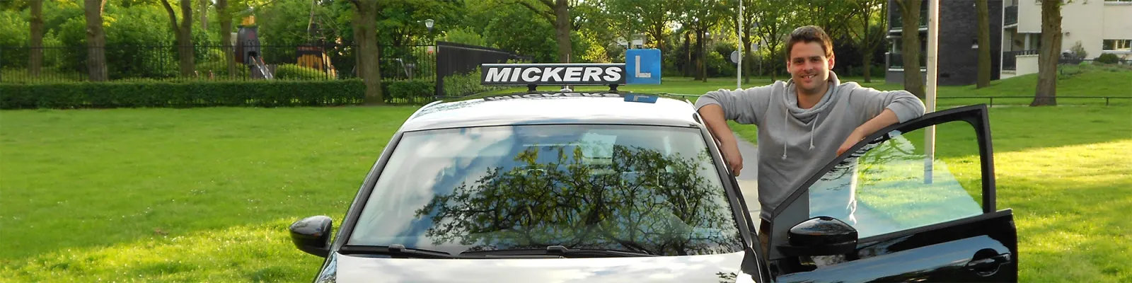 Michel Mickers staat naast een lesauto van Mickers Rijopleidingen in een park
